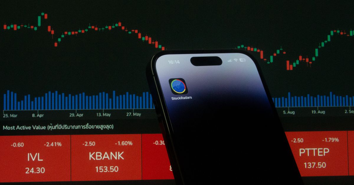 lloyd blankfein trading - A mobile phone displaying a trading app in front of a financial market chart screen.