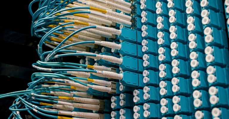 green bond market - Detailed view of fiber optic patch cables connecting to a blue patch panel in a data center.