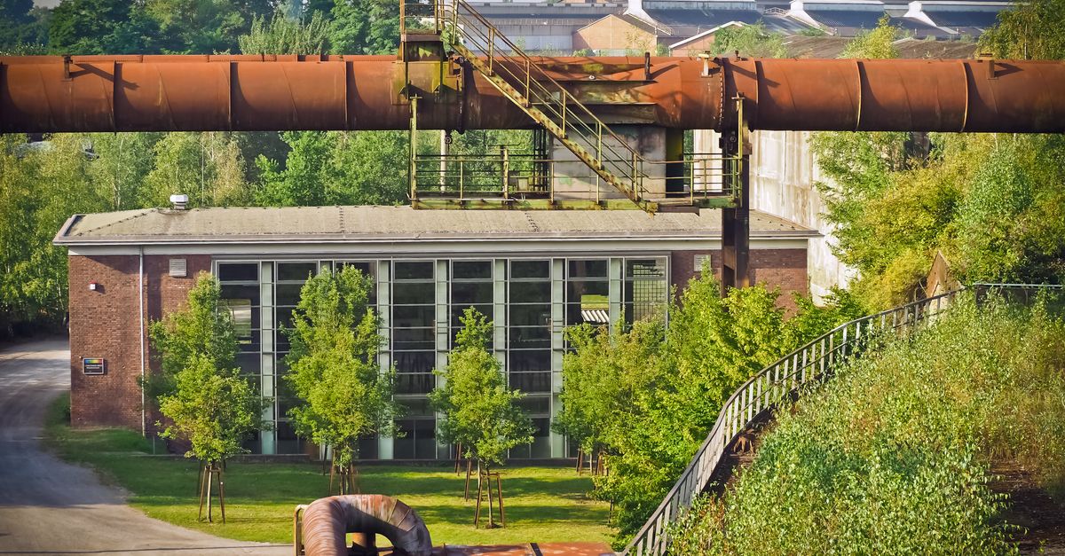 green steel plant - A scenic view of an old industrial plant with rusty pipes and surrounding greenery in daylight.