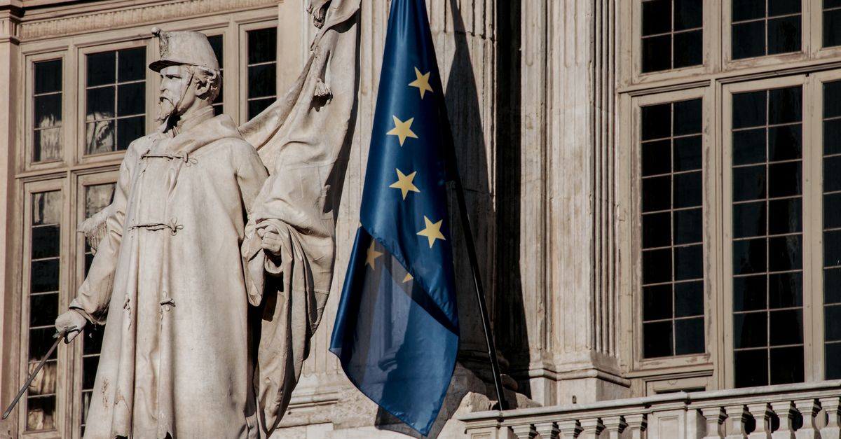 binance eu mica rules - European Union flag waving beside a historic statue on stone building facade.