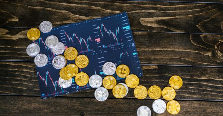 mica compliant crypto - Gold and silver cryptocurrency coins scattered on a trading chart over a wooden table.