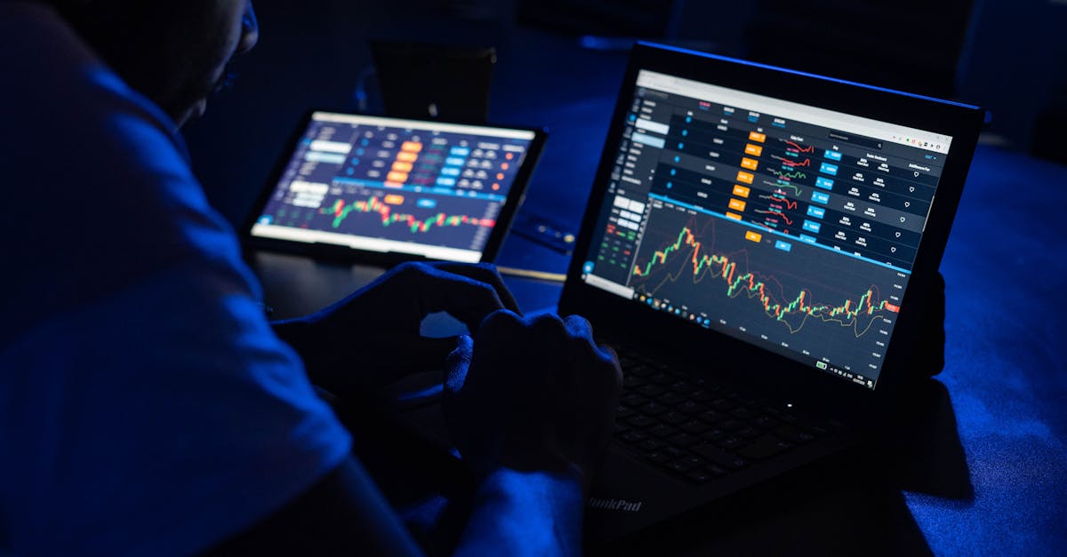 robo-advisers ai - Man analyzing financial charts and data on laptops in a dimly lit room, highlighting forex trading.