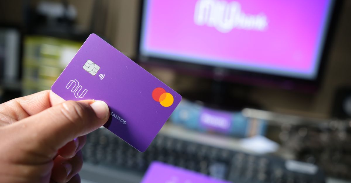 neobank challenger bank - A close-up of a hand holding a purple bank card in front of a computer screen.
