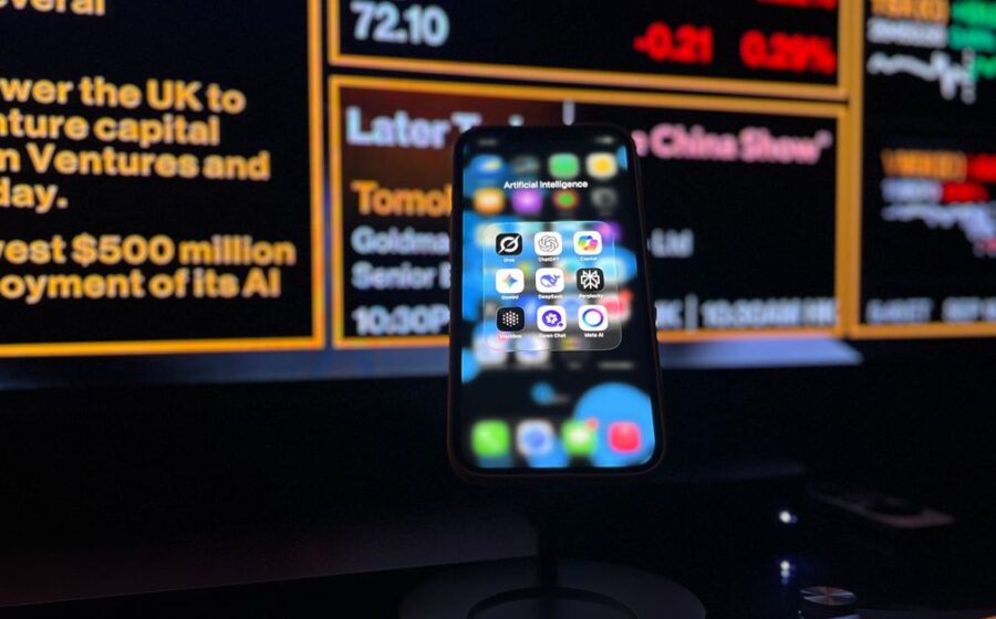 ai investment bust - Smartphone displaying AI apps in front of a financial data screen in London.
