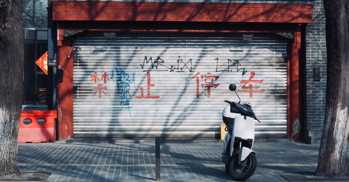alibaba ant settlement - A scooter parked in front of a graffiti-covered shuttered shop on a sunny urban street.