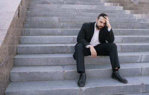 Man in suit sitting on outdoor stairs looking down.