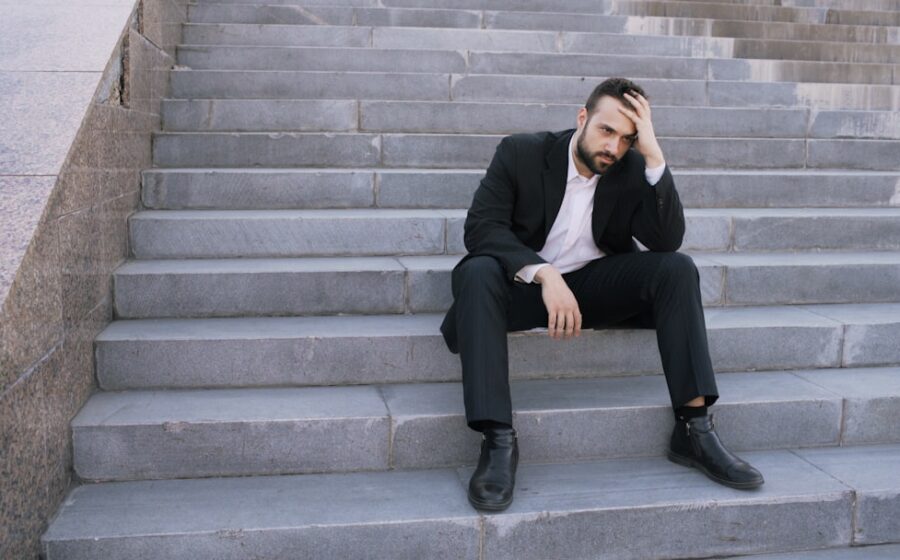 Man in suit sitting on outdoor stairs looking down.