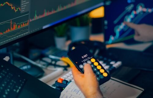 embat global banking - Trader analyzing stock market charts on computer screens with calculator.
