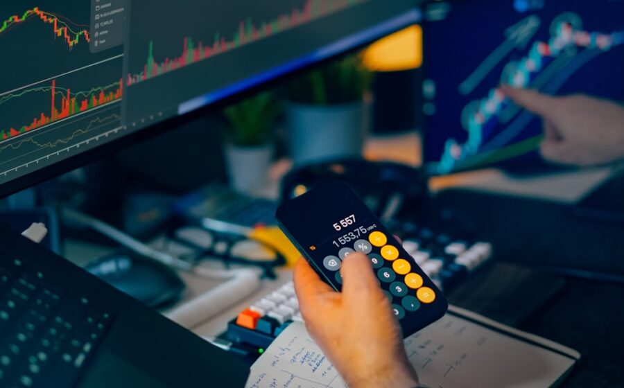embat global banking - Trader analyzing stock market charts on computer screens with calculator.
