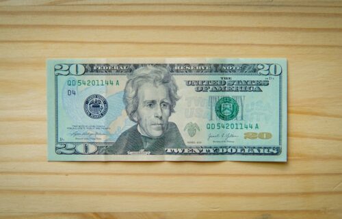 debit interchange plan - A twenty-dollar bill rests on a light wooden background.