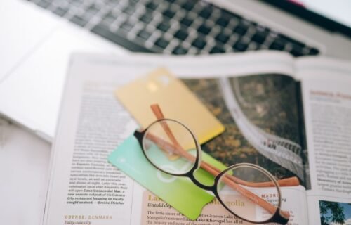 cross border payments - Overhead view of reading glasses, credit cards, and a magazine with a blurred laptop in the backgroun
