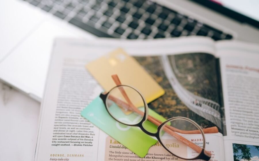 cross border payments - Overhead view of reading glasses, credit cards, and a magazine with a blurred laptop in the backgroun