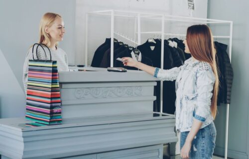 stripe paypal offer - A woman paying by card at a store counter, handing card to female cashier.