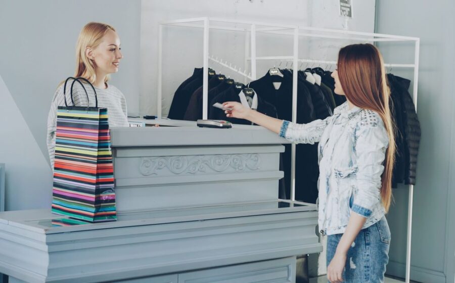 stripe paypal offer - A woman paying by card at a store counter, handing card to female cashier.