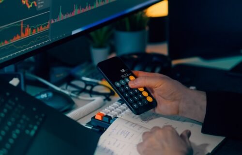 ESG investing sustainable finance - Person using calculator at desk with computer charts.