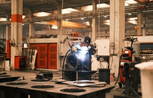 ai boom manufacturing - A man welding a piece of metal in a factory