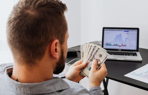 berkshire hathaway profit - Man counting money at a desk with a laptop showing financial data.