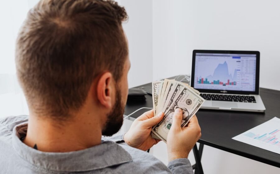 berkshire hathaway profit - Man counting money at a desk with a laptop showing financial data.