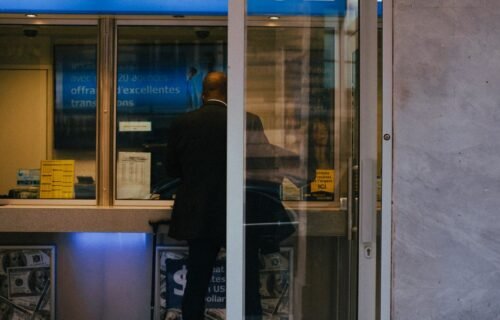 ai risks banking - Man at a currency exchange office window, showing currency rates inside a bustling city.