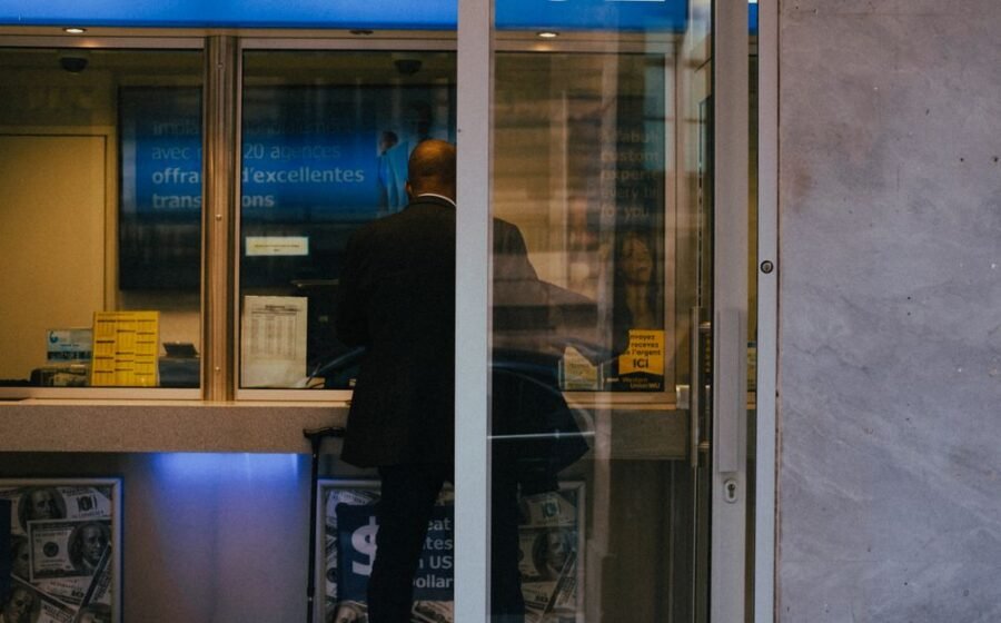 ai risks banking - Man at a currency exchange office window, showing currency rates inside a bustling city.