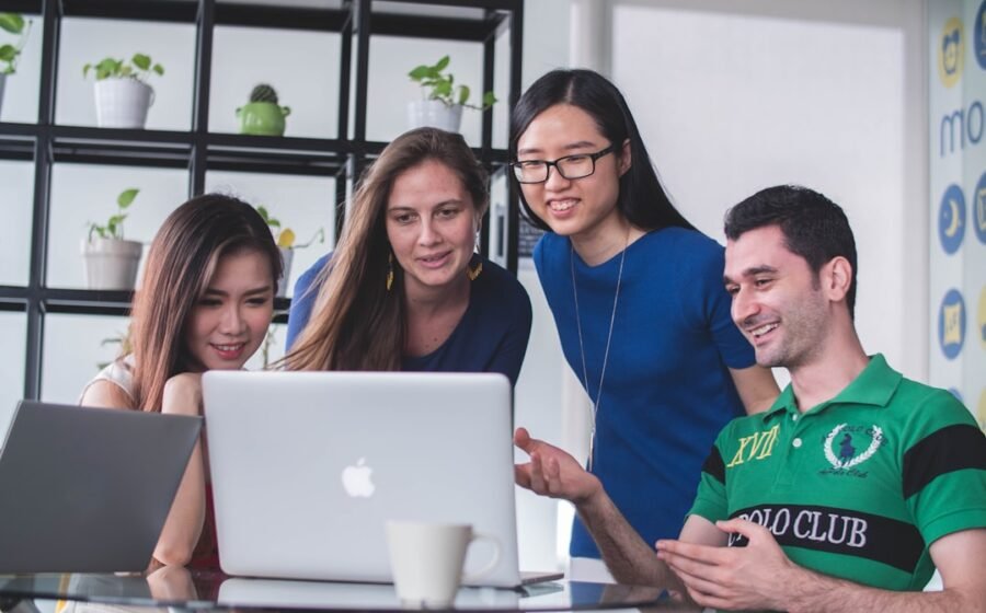 fintech tools for startups - four people watching on white MacBook on top of glass-top table