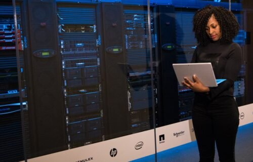 bitcoin mining operations - A female engineer using a laptop while monitoring data servers in a modern server room.