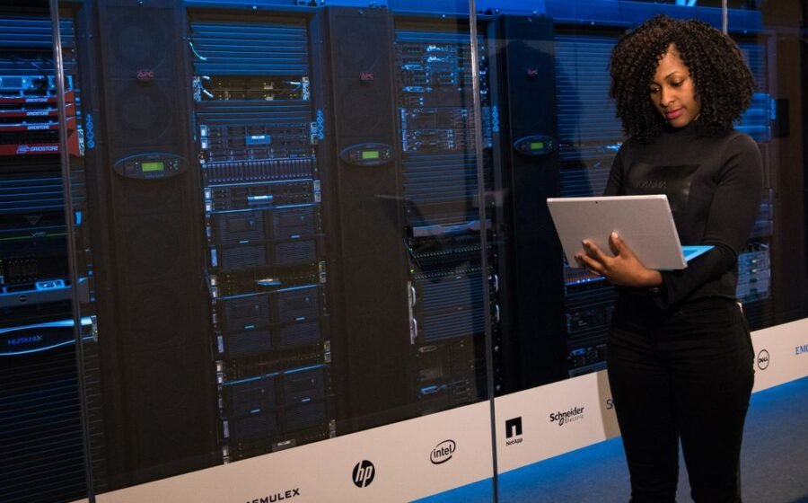 bitcoin mining operations - A female engineer using a laptop while monitoring data servers in a modern server room.