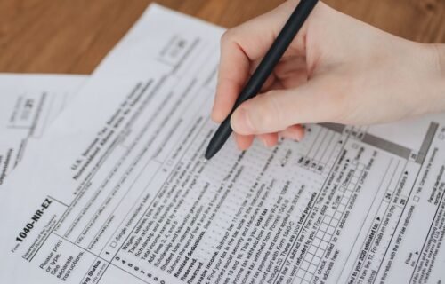 fincen smuggling data - Close-up of a hand writing on tax documents with a black pen.