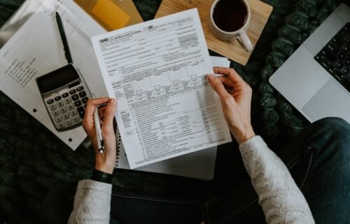 invoice financing - Hands holding tax forms with calculator and laptop.