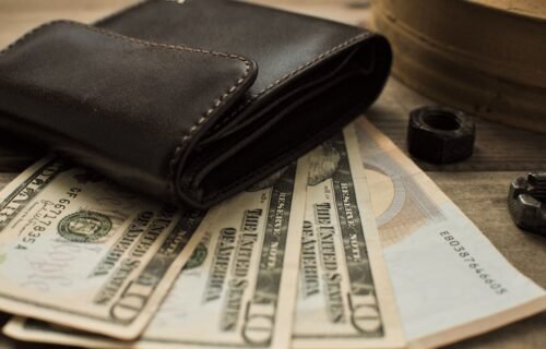 high-end spending - Close-up view of a leather wallet with US dollar bills on a wooden table.