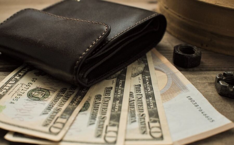 high-end spending - Close-up view of a leather wallet with US dollar bills on a wooden table.