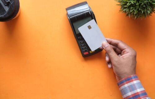 card fraud threats - A person holding a blank credit card near a payment terminal on orange