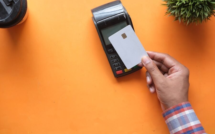 card fraud threats - A person holding a blank credit card near a payment terminal on orange